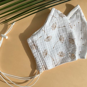 May include: Two white face masks with adjustable straps. One mask has a gold dandelion print and the other has gold dots.