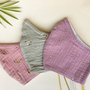 May include: Three reusable face masks with gold accents. One mask is light brown with a gold floral pattern, one is pink with a gold floral pattern, and one is pink with gold dots.
