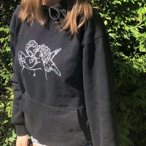 Pu&ograve; includere: Felpa nera con un design di due angeli che si abbracciano in strass bianchi.