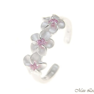 Puede incluir: Anillo de plata con tres flores blancas de plumeria con centros de cristal rosa. El anillo es ajustable.