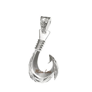 May include: Silver Hawaiian fish hook pendant with intricate engraved designs. The hook is curved and has a detailed bail. The pendant is inscribed with the words "Man Loa".