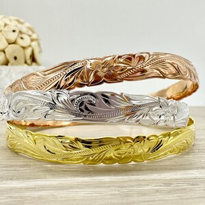 May include: Three Hawaiian flower lei bracelets in gold, silver, and rose gold. The bracelets are stacked on top of each other.