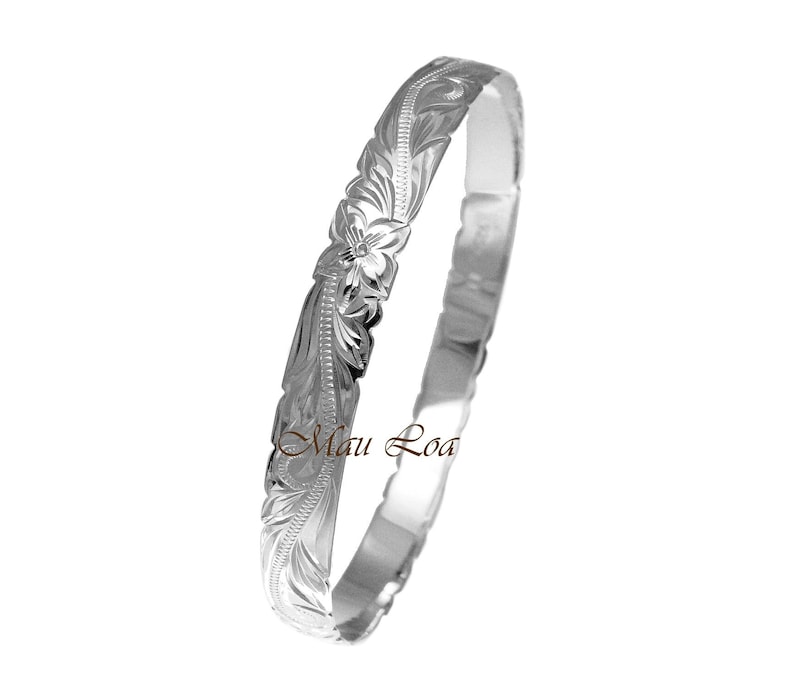 May include: A silver bangle bracelet with a floral design. The bracelet is engraved with the words "Maui Loa".