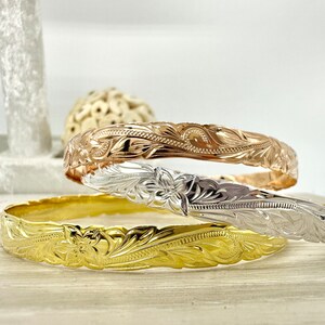 May include: Three gold, silver, and rose gold Hawaiian bracelets with intricate floral designs.