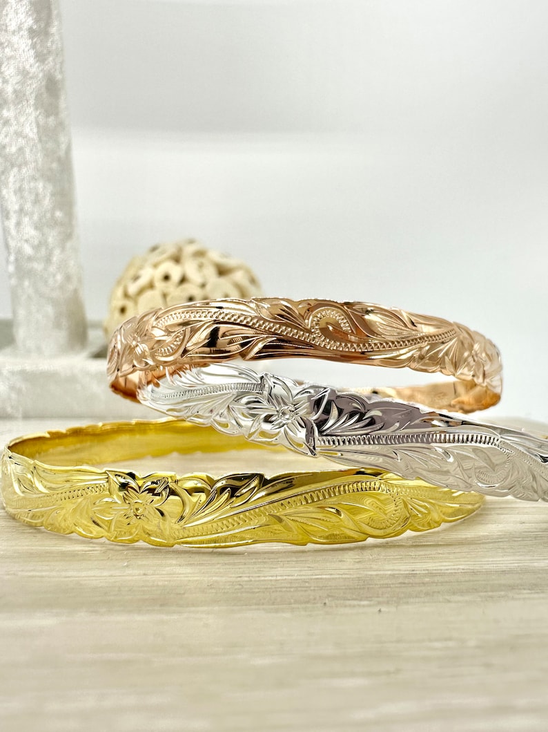 May include: Three gold, silver, and rose gold Hawaiian bracelets with intricate floral designs.