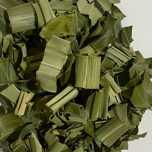 May include: Close-up of dried, chopped green leaves. The leaves are a muted green color and appear to be cut into various sizes. The texture of the leaves is visible, with prominent veins. The image is well-lit, highlighting the natural color and texture of the leaves.