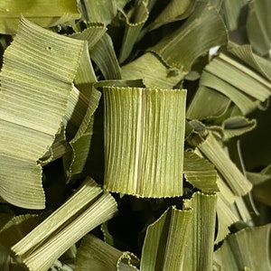 May include: Close-up of dried, pale green pandan leaves. The leaves are cut into strips and have a textured, ribbed appearance. The image shows a pile of the leaves, with some curled and folded.