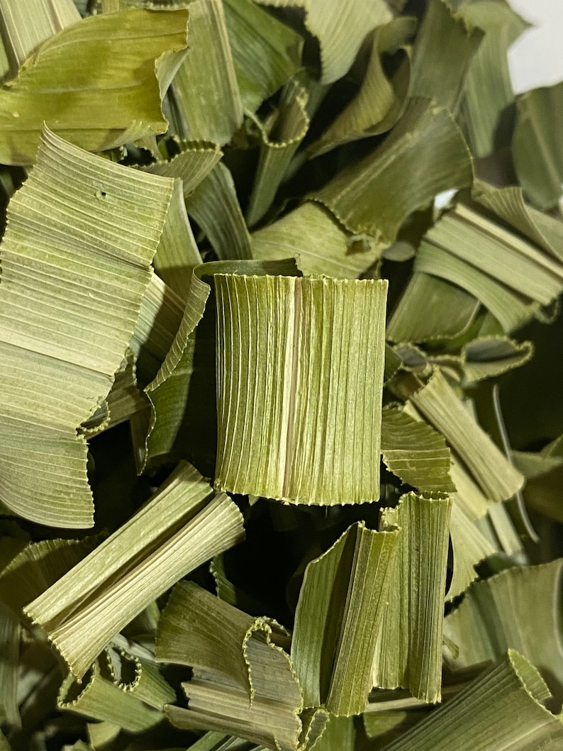 May include: Close-up of dried, pale green pandan leaves. The leaves are cut into strips and have a textured, ribbed appearance. The image shows a pile of the leaves, with some curled and folded.