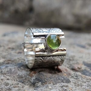 May include: A silver ring with a textured band and a green gemstone set in the center. The band is decorated with a floral pattern.