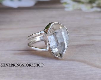 May include: A silver ring with a clear quartz gemstone. The ring has a double band and the gemstone is faceted.