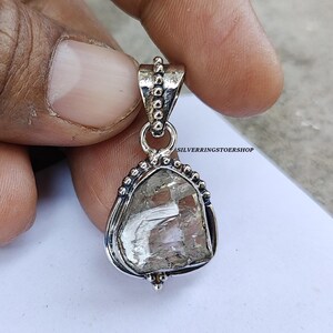 May include: A silver pendant featuring a clear, faceted crystal set in a silver frame with a beaded border. The pendant is attached to a silver bail with a beaded design. The text "SILVERRINGSTOERSHOP" is visible in the background.