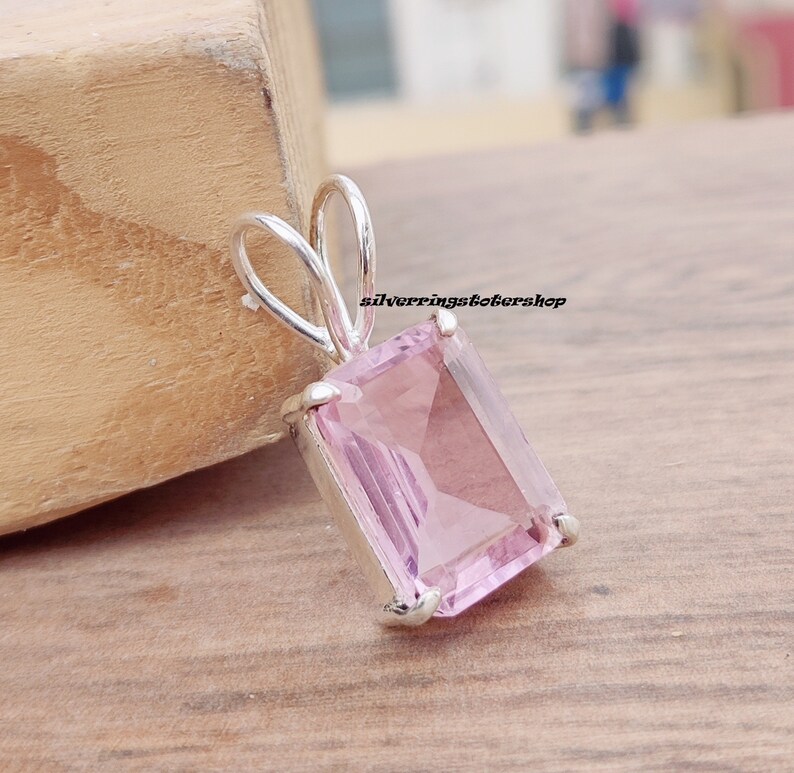 May include: A silver pendant with a light pink rectangular gemstone. The pendant has a bail for attaching to a chain.