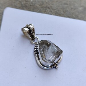 May include: A silver pendant featuring a clear quartz crystal set in a silver frame with beaded accents. The pendant is on a white background.  "SILVERRINGSTOERSHOP" is printed on the background.