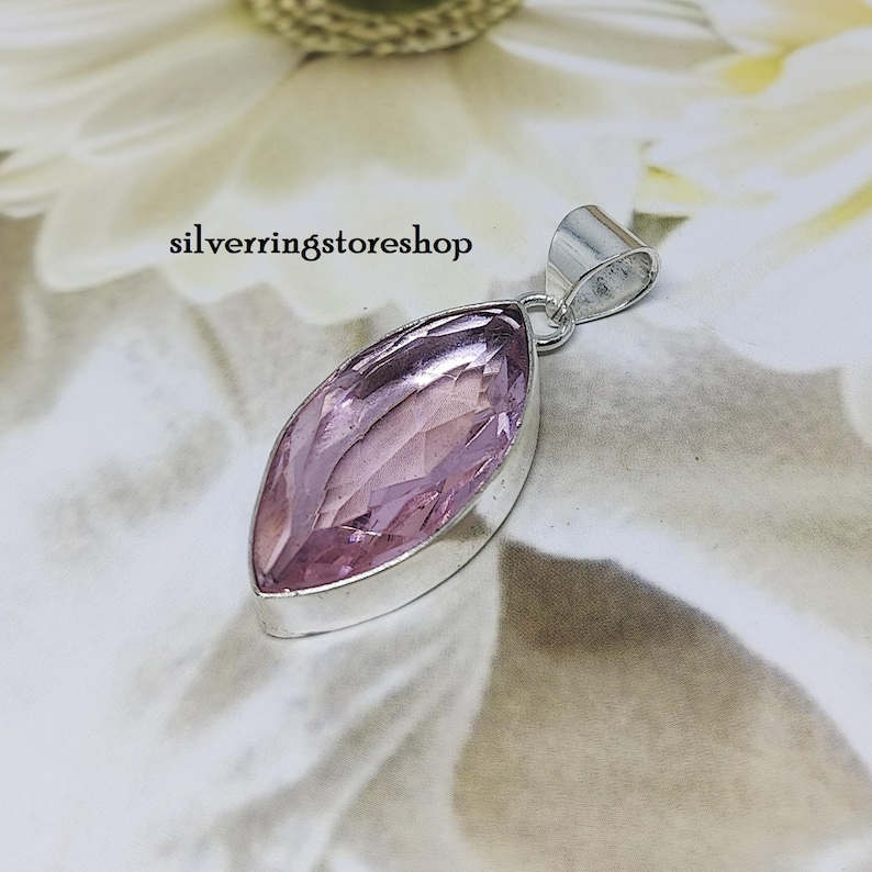 May include: A silver pendant with a light pink marquise-shaped gemstone. The pendant is on a white background.