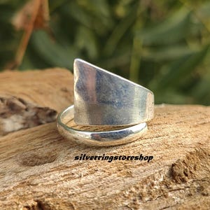 May include: A silver ring with a unique design. The ring is made of two pieces of metal that are joined together. The top piece is a flat, triangular shape that wraps around the bottom piece. The ring is a simple and elegant design.