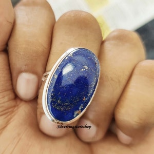 May include: A silver ring with a large oval lapis lazuli gemstone. The stone is a deep blue color with gold flecks throughout. The ring is set in a simple silver band.