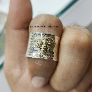 May include: A silver hammered band ring with a gold bee design. The ring is worn on a finger.