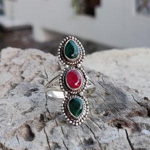 Peut inclure: Une bague en argent avec trois pierres précieuses. Les pierres du haut et du bas sont vertes, et la pierre du milieu est rouge.
