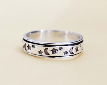 May include: A silver spinning ring with a design of moons and stars around the band.