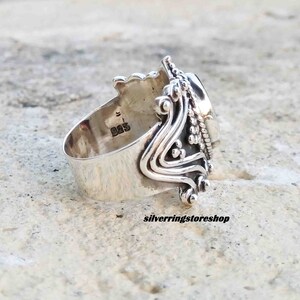 Puede incluir: Un anillo de plata con un dise&ntilde;o ornamentado y una gran piedra ovalada. El anillo est&aacute; marcado con "925" en la banda interior.