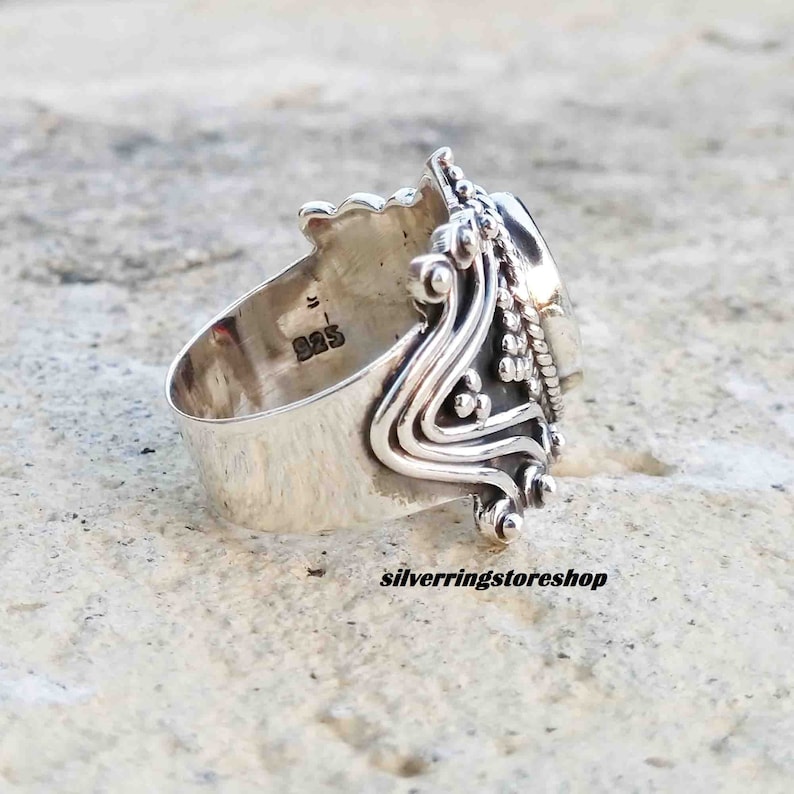 Puede incluir: Un anillo de plata con un dise&ntilde;o ornamentado y una gran piedra ovalada. El anillo est&aacute; marcado con "925" en la banda interior.