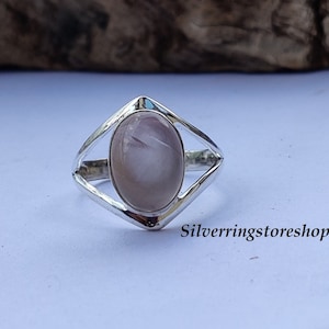 May include: A silver ring with a light pink oval gemstone set in a geometric design. The ring features a polished finish and the text "Silverringstore shop" is visible.