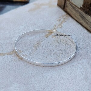 May include: A silver hammered bangle bracelet. The bracelet is thin and has a smooth, polished finish.