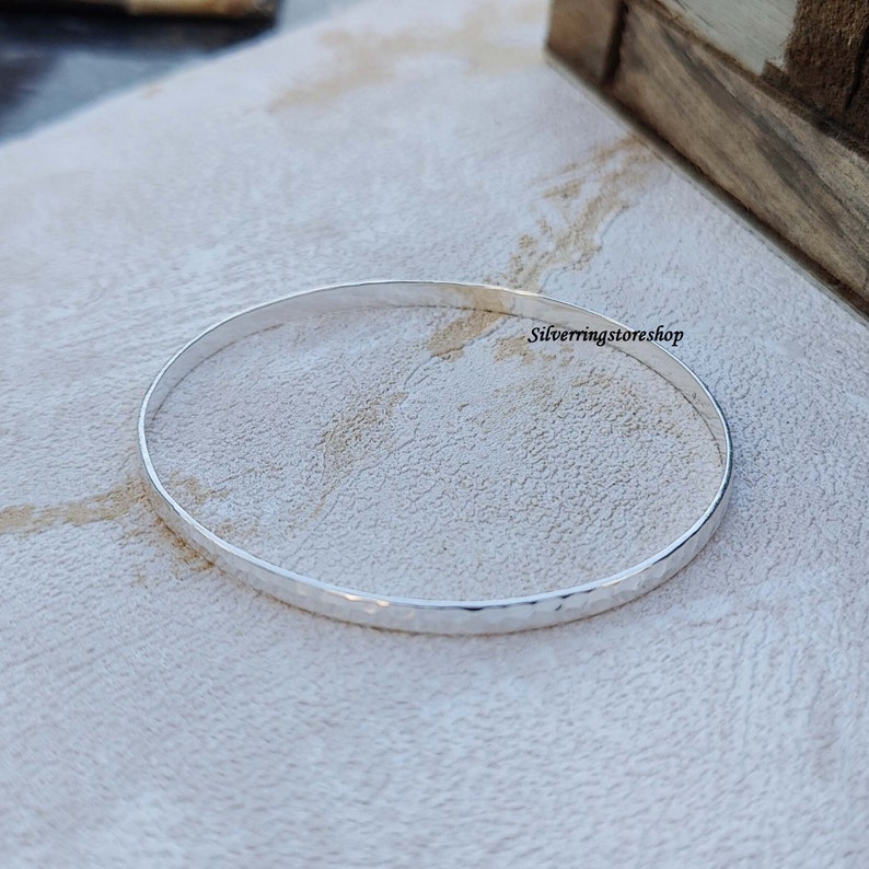 May include: A silver hammered bangle bracelet. The bracelet is thin and has a smooth, polished finish.