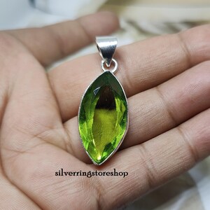 May include: A silver pendant featuring a large, faceted, green gemstone in a marquise shape.