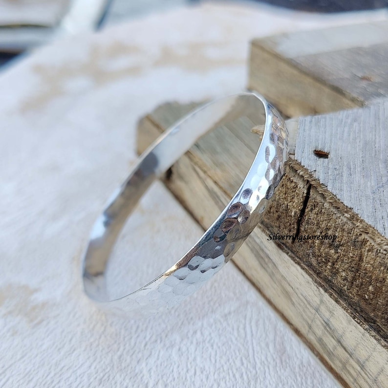 May include: A silver hammered bangle bracelet. The bracelet is smooth and shiny, with a hammered texture.