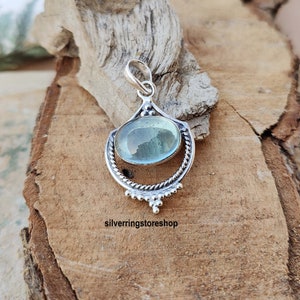 May include: A silver pendant with a light blue oval gemstone set in a decorative silver frame. The pendant has a bail for attaching to a chain.