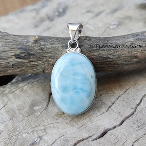 May include: A silver pendant featuring a light blue oval cabochon gemstone. The gemstone has a swirling, marbled pattern.