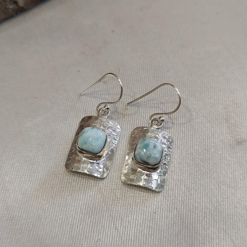 Pode incluir: Um par de brincos de prata com uma gema azul claro engastada em uma moldura de prata texturizada. Os brincos t&ecirc;m um fecho de gancho simples.