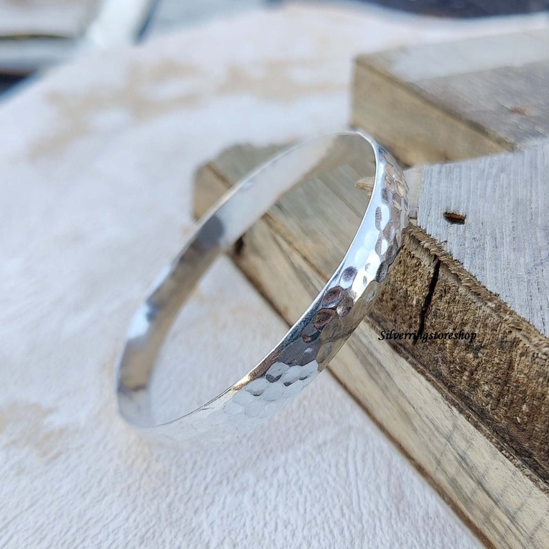 May include: A silver hammered bangle bracelet. The bracelet is smooth and shiny, with a hammered texture.