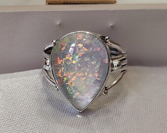 Può includere: Un anello d'argento con una pietra di opale iridescente a forma di pera. L'opale mostra colori come arancione, verde e blu. L'anello ha un design dettagliato a più bande.