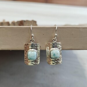 Pode incluir: Brincos de prata com uma gema azul claro engastada em uma moldura de prata martelada.