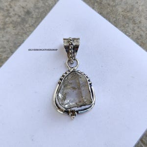May include: A silver pendant featuring a clear quartz crystal set in a silver bezel with a beaded border. The pendant has a silver bail for attaching to a chain.