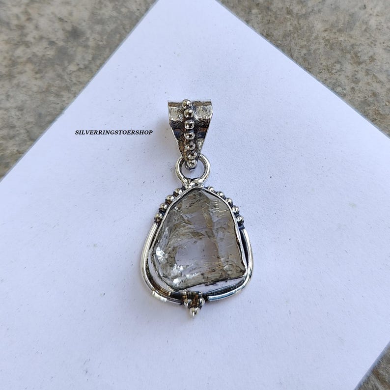 May include: A silver pendant featuring a clear quartz crystal set in a silver bezel with a beaded border. The pendant has a silver bail for attaching to a chain.