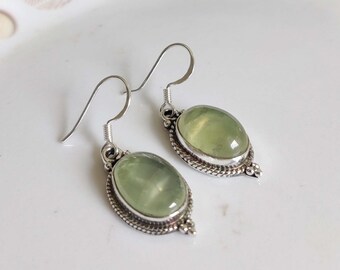 May include: A pair of silver earrings with green gemstone oval drops. The earrings have a delicate silver design around the stones.