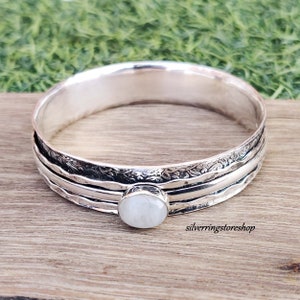 Op de afbeelding: Zilveren armband met drie banden en een witte maansteen cabochon. De armband heeft een gehamerde textuur en bloemmotieven.