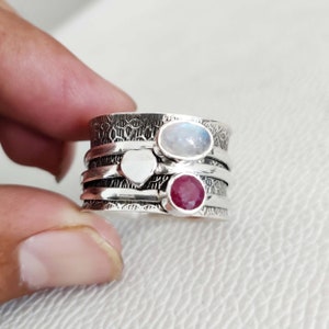 Op de afbeelding: Een draaibare zilveren ring met drie stenen: een witte hartvormige steen, een witte ovale maansteen en een rode robijn.