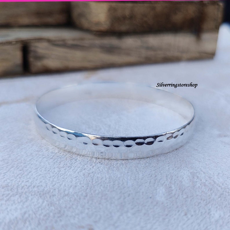 May include: A silver bangle bracelet with a hammered texture. The bracelet is simple and elegant.