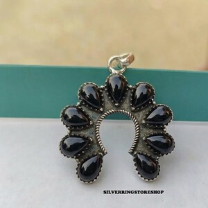 Pu&ograve; includere: Ciondolo in argento a forma di ferro di cavallo, ornato con pietre nere a forma di goccia. Il ciondolo ha una finitura strutturata e ossidata e un piccolo anello per una catena. Il testo "SILVERRINGSTORESHOP" &egrave; visibile in basso.