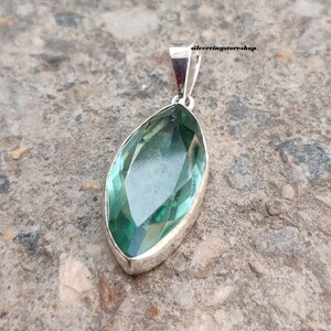 May include: A silver pendant with a large, faceted, green gemstone. The gemstone is shaped like a marquise and has a high polish.
