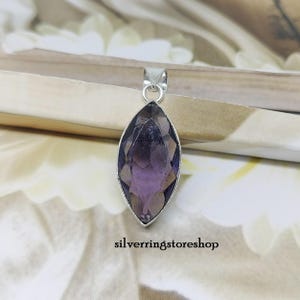 May include: A silver pendant with a marquise-shaped amethyst gemstone. The gemstone is a deep purple color and has a faceted cut.