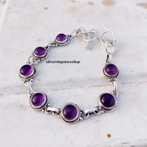 May include: A silver bracelet featuring seven round, deep purple gemstones. Each stone is set in a decorative, beaded bezel. The bracelet has a toggle clasp and is displayed on a light-colored surface. The text "silverringstore shop" is visible.