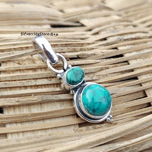May include: A silver pendant with two turquoise stones. The larger stone is oval-shaped and the smaller stone is round. The pendant has a bail for attaching to a chain.