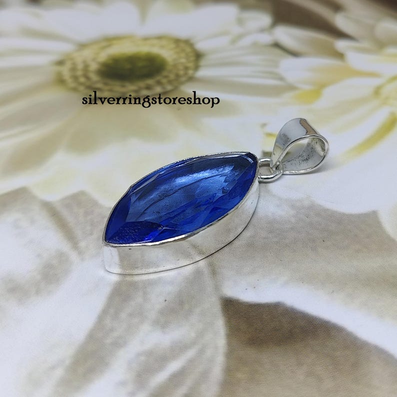 May include: A silver pendant with a marquise-shaped blue gemstone. The pendant is set in a silver bezel and has a bail for attaching to a chain.