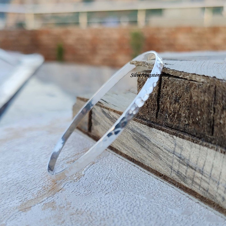 May include: A silver hammered bangle bracelet. The bracelet is made of sterling silver and has a smooth, polished finish.