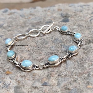 May include: A silver bracelet featuring oval and round light blue gemstones. The gemstones are set in ornate silver bezels and linked by a chain. The bracelet has a toggle clasp. The text "silverringstore shop" is visible.